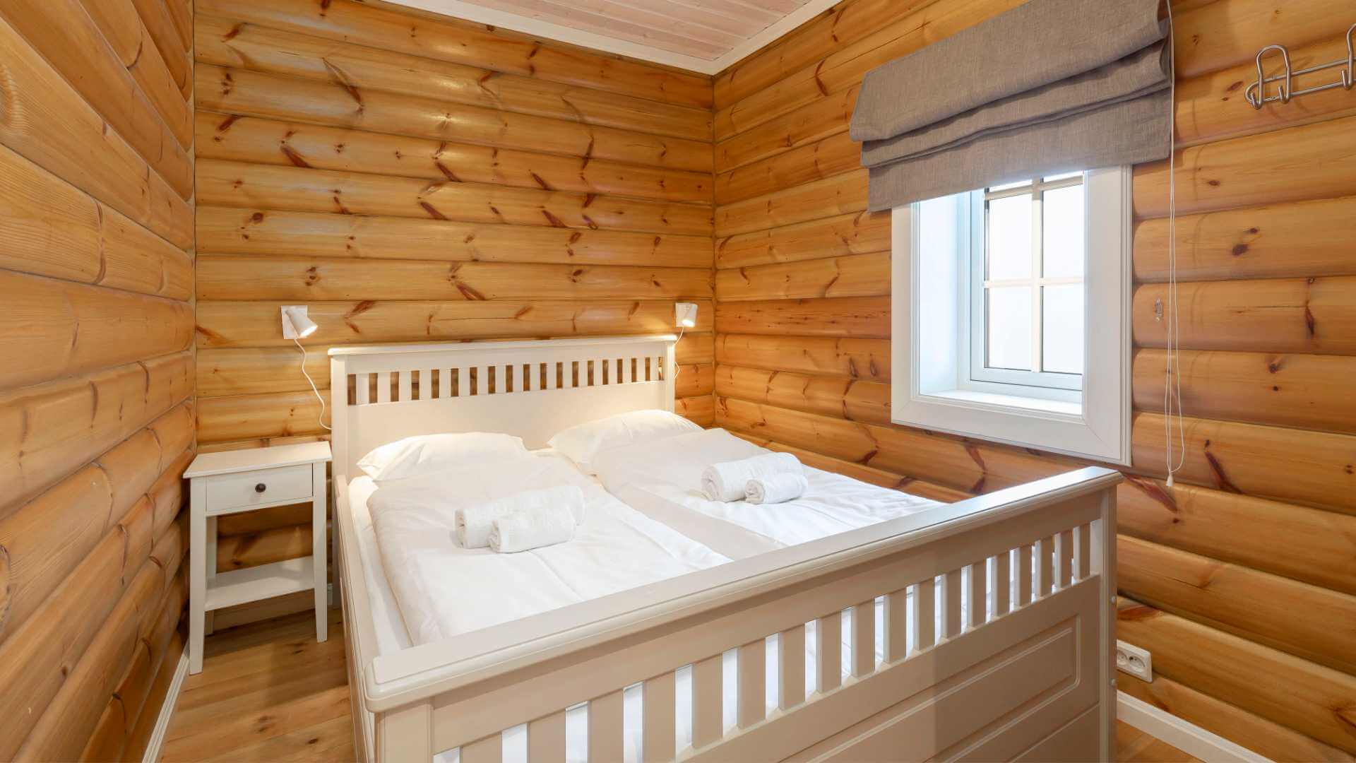 Soverom med dobbeltseng i tømmerhytte, lyse vegger og vindu med gardin.