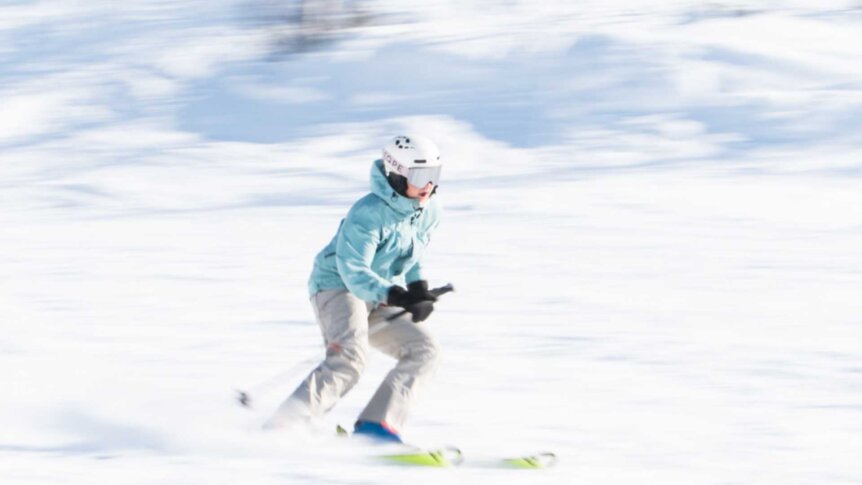 Person som står på ski i snødekt terreng, iført hjelm og blå jakke.
