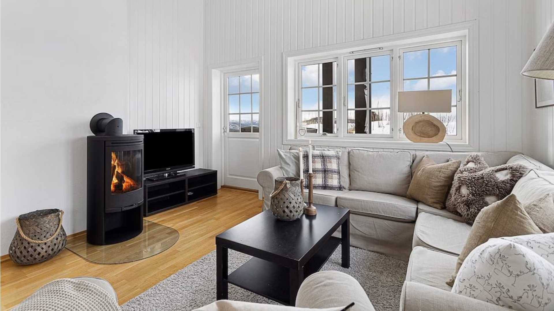 Lyst og koselig stue med peis, sofa, moderne TV og store vinduer med utsikt. Perfekt for avslapning.
