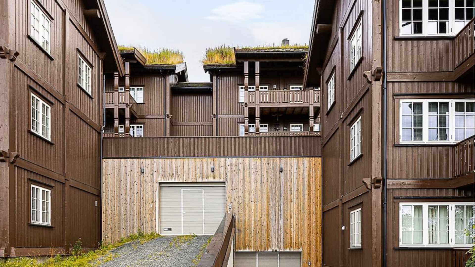Moderne brune bygninger med grønne tak, en trapp opp til garasje, omgitt av natur. Ideelt for bolig- eller ferieopphold.
