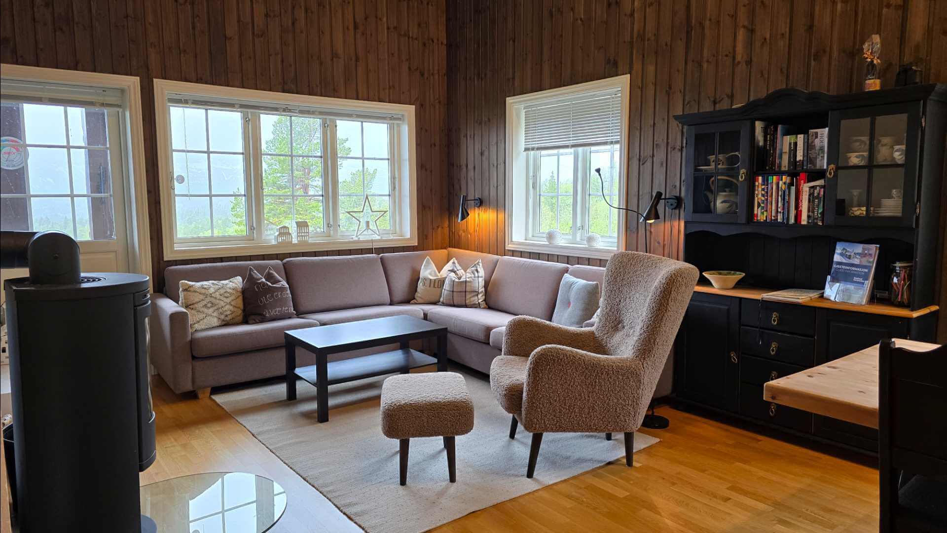 Koselig stue med moderne sofa, stol og naturlig lys fra vinduene, omgitt av trevegg og stilfulle interiørdetaljer.