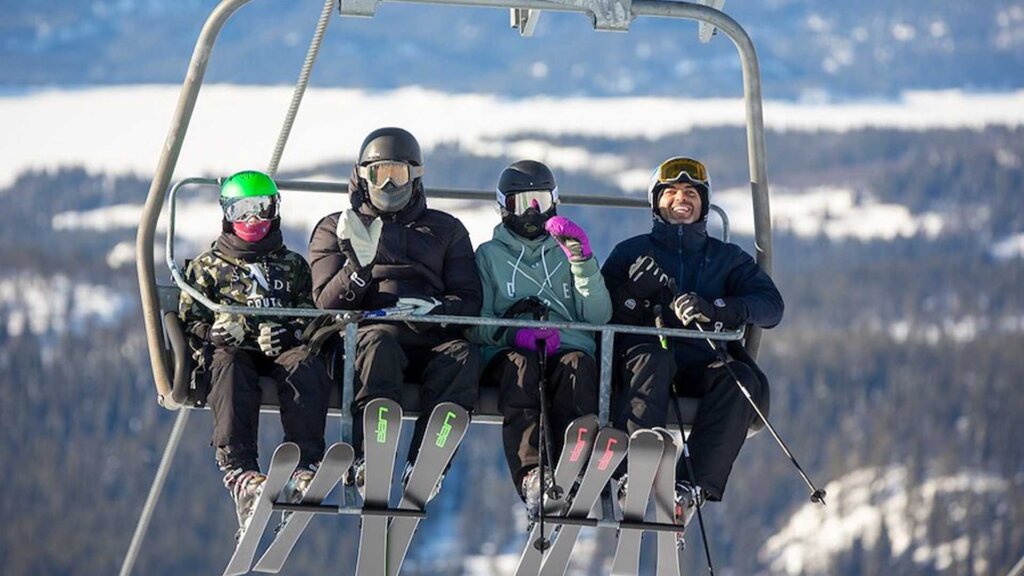 Familie på skitrekk, klare for en dag med moro i bakken, omringet av snødekte fjell.