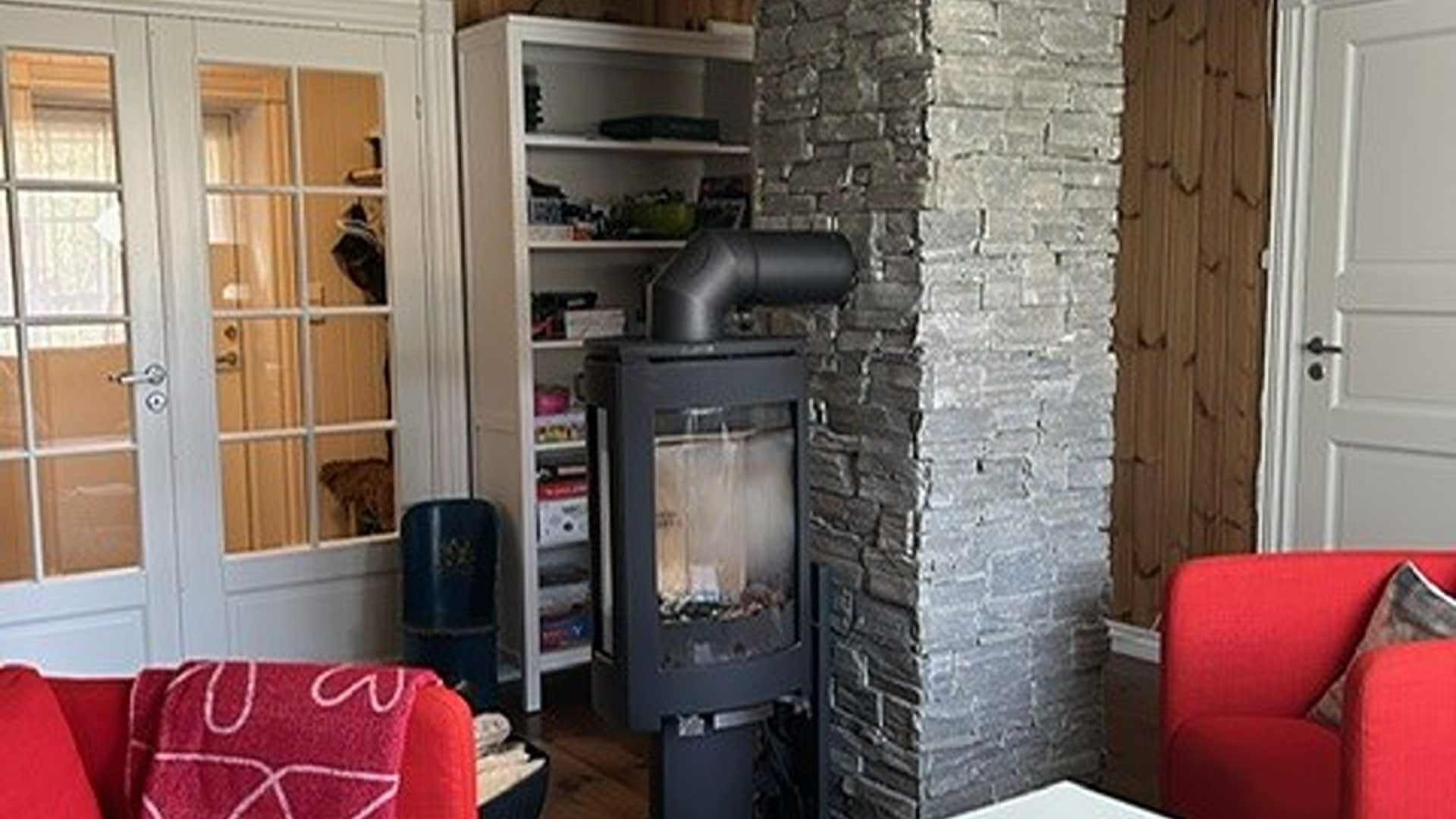 Kosefull stue med peis, røde sofaer og bokhyller, med dører i glass som fører til et rom.