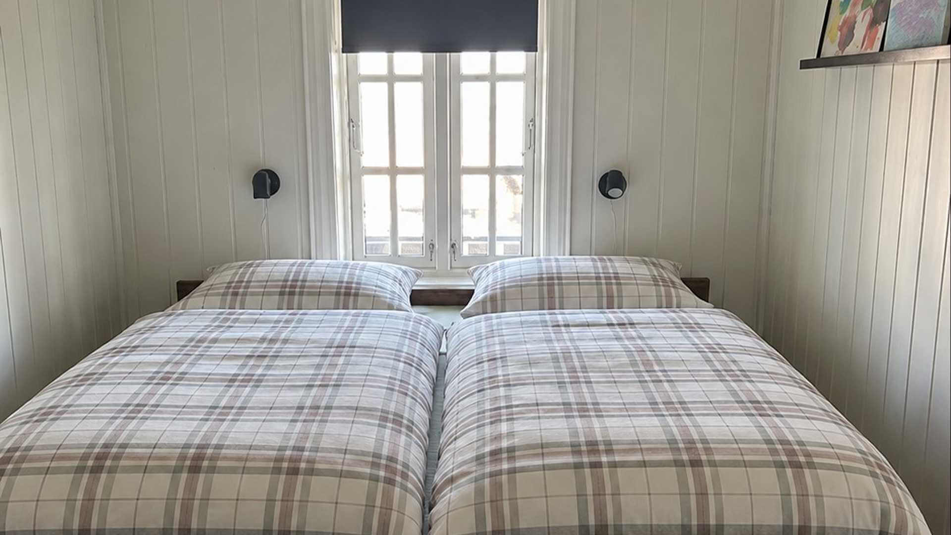 Lyst soverom med to enkelt senger, rute mønster og vindu som slipper inn naturlig lys.