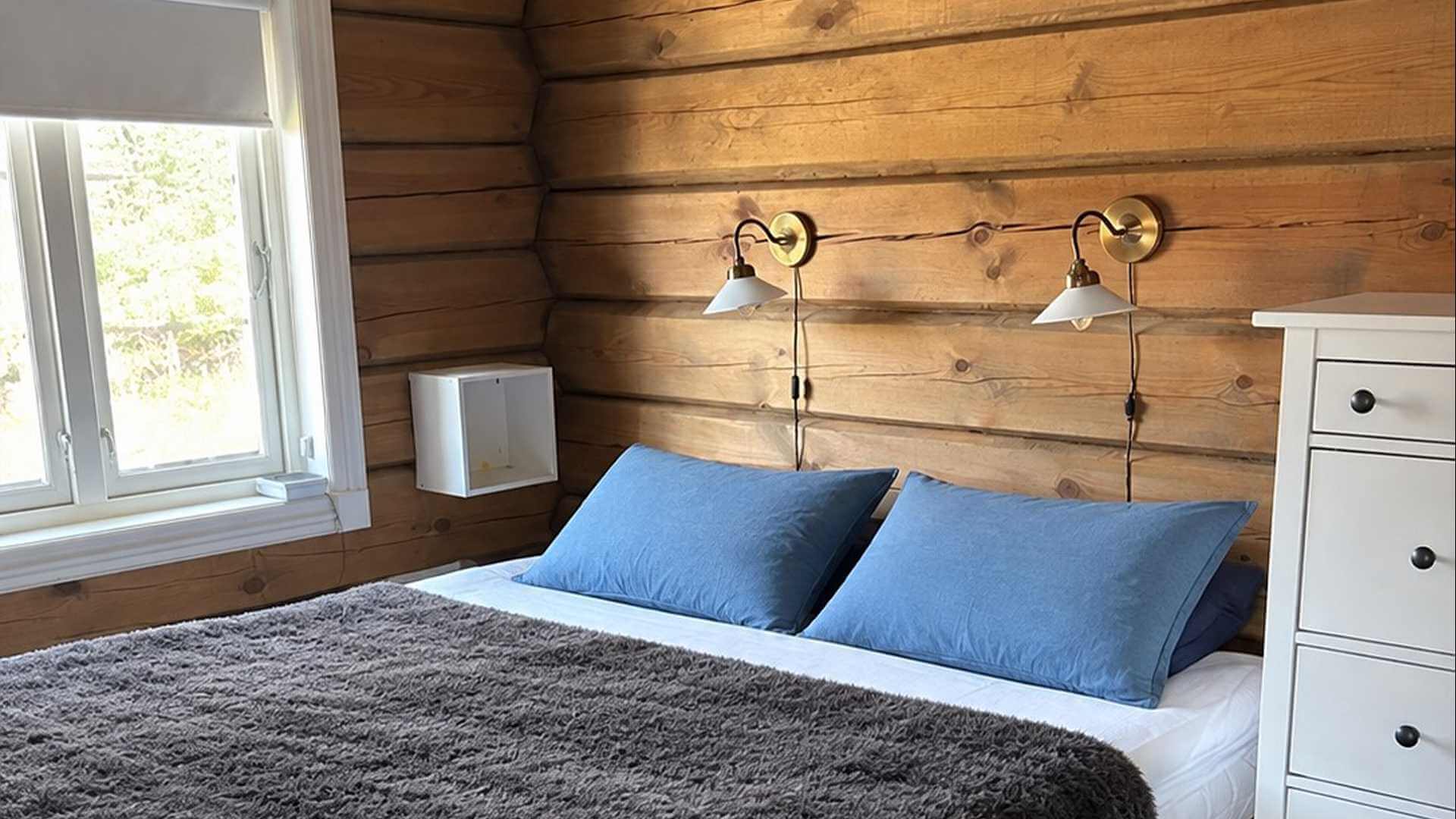 Koselig soverom med trevegger, to blå puter, en myk teppe og moderne lamper. Perfekt for avslapning.