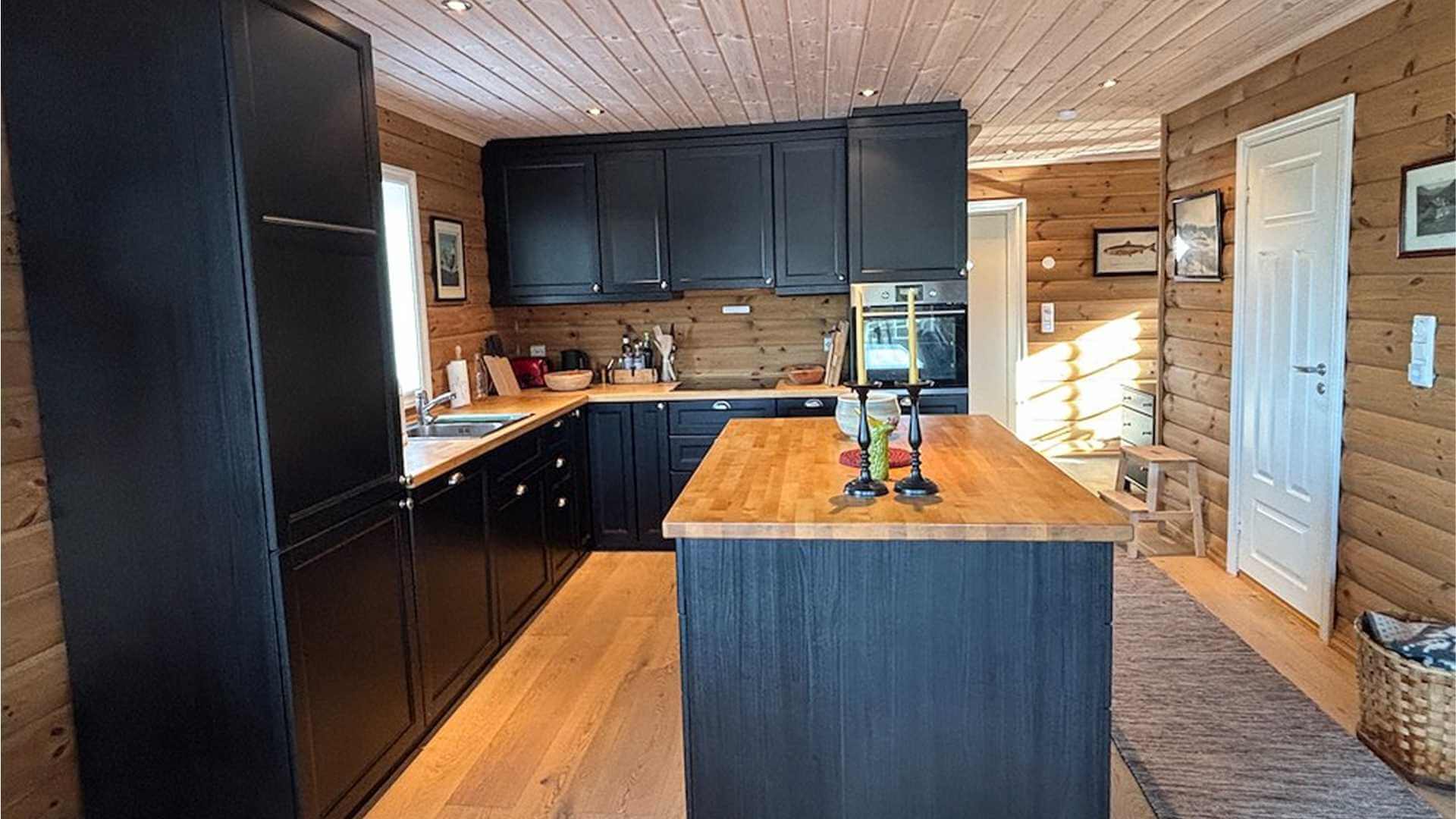Moderne kjøkken med svart skap, trebenk og naturlig lys i en koselig hytte. Ideelt for matlaging og samvær.