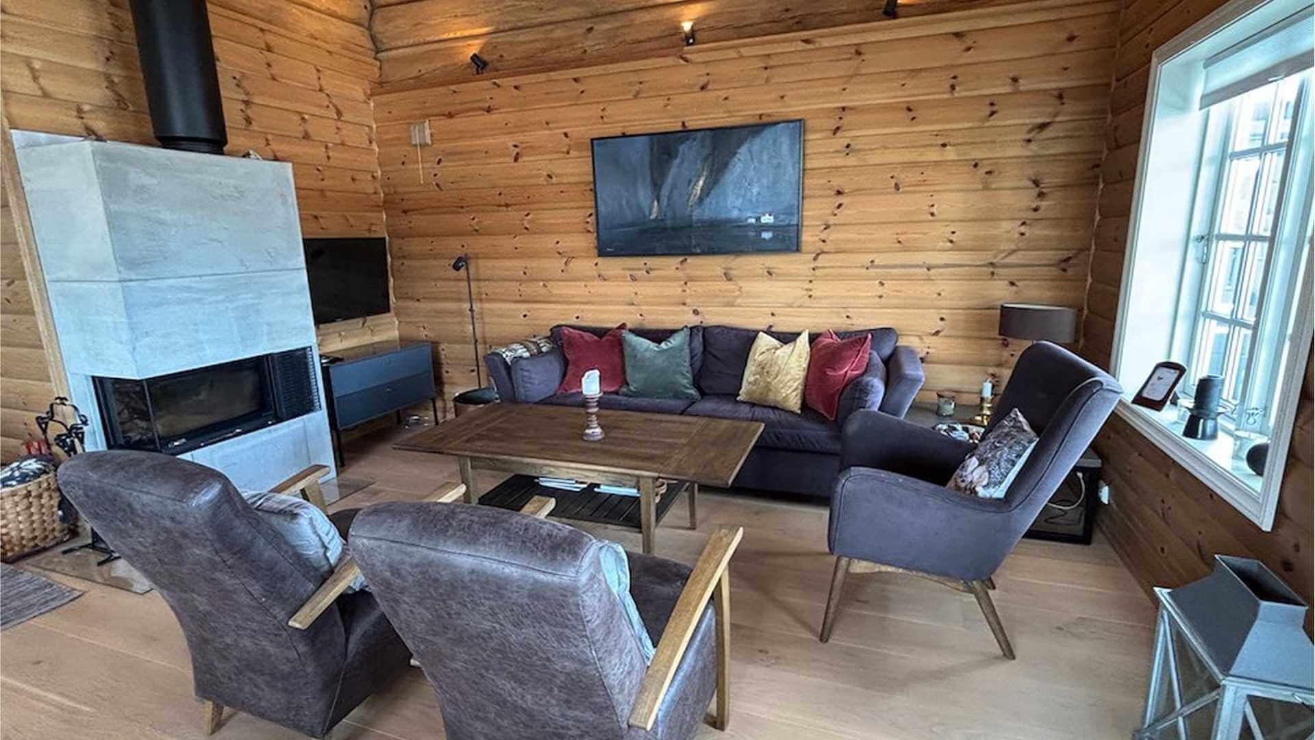 Lyst og moderne stue med peis, komfortable stoler og en koselig atmosfære i tømmerhus.