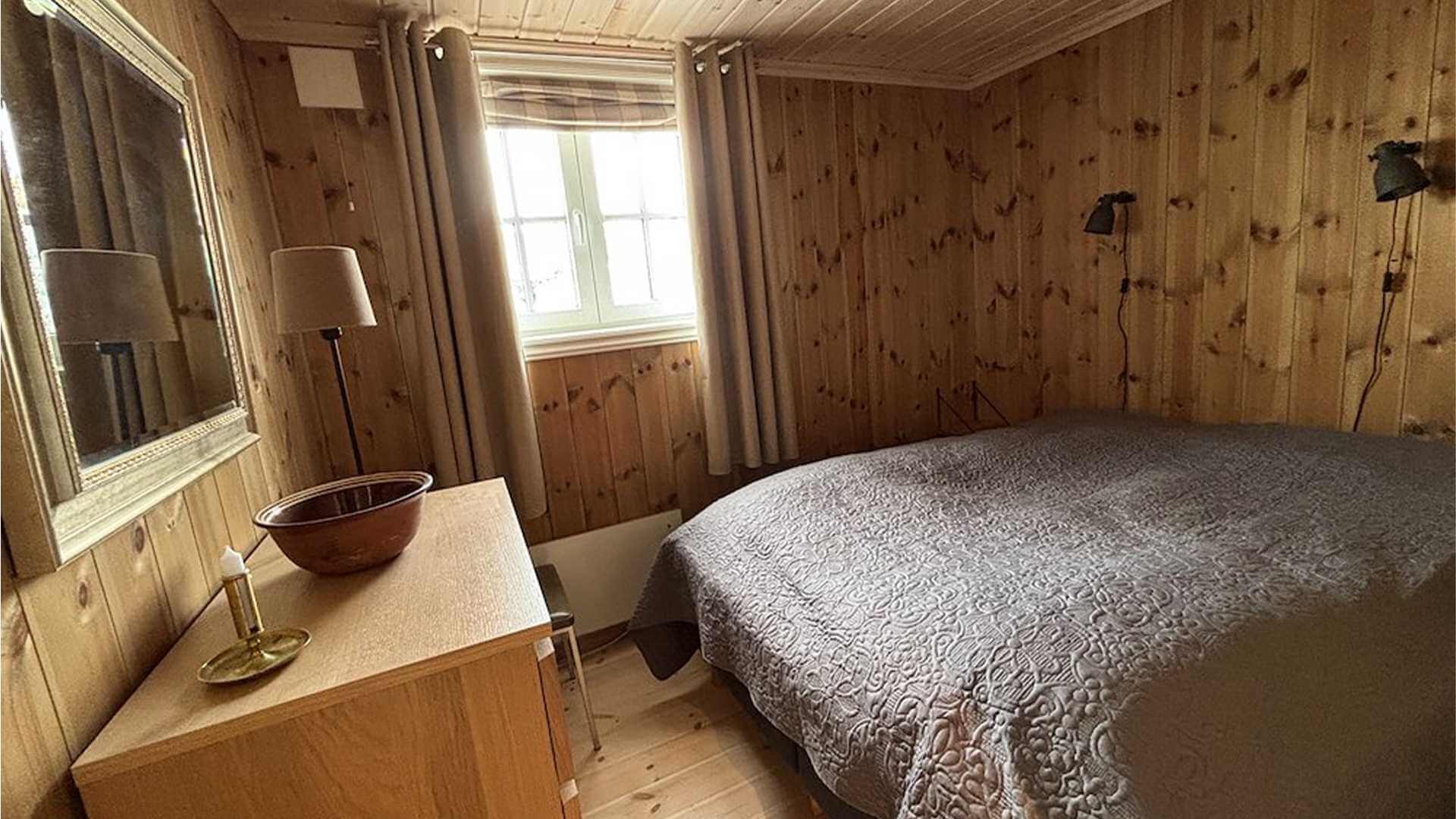Koselig soverom med trevegg, stor seng, speil og stilig belysning i naturlige farger. Ideelt for avslapning.