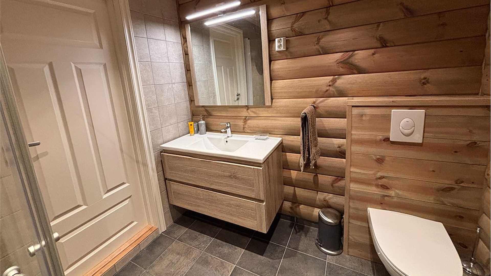 Moderne baderom med trevegg, servant, speil og toalett i naturmaterialer. Ren og stilfull innredning.