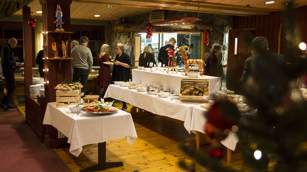 Julebuffet med gjester i en koselig restaurant, med tradisjonell skandinavisk dekor og mat.