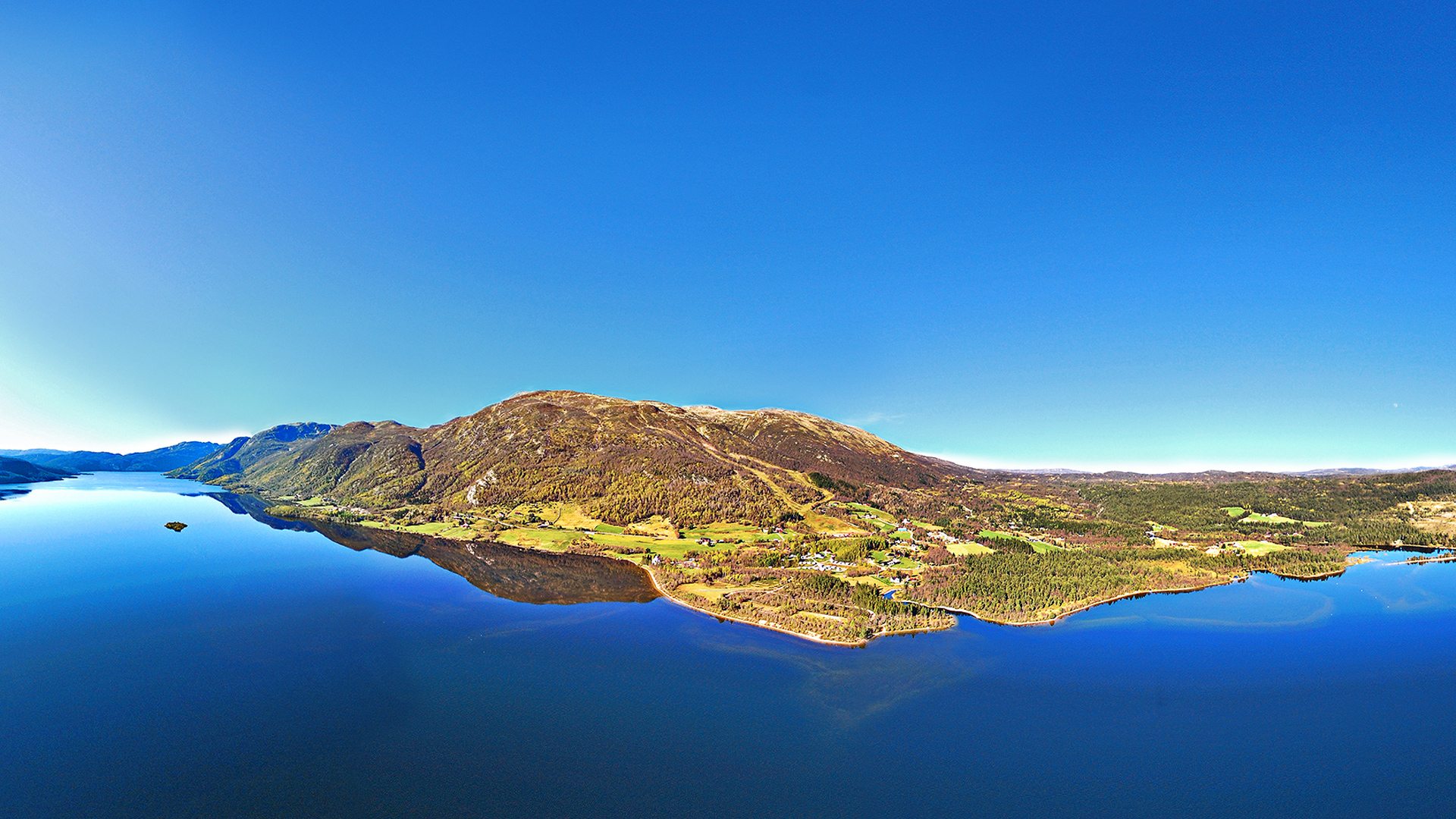 Panoramautsikt over en fjord og fjell i Norge under klar blå himmel.