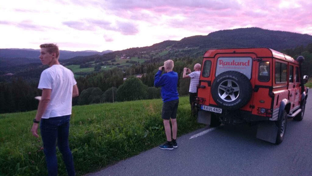 Tre personer ser på solnedgangen i Rauland med en rød bil parkert langs veien.
