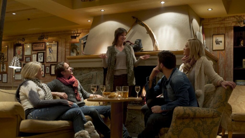 Gruppe venner samlet foran peis, prater og nyter drikke i koselig stue.