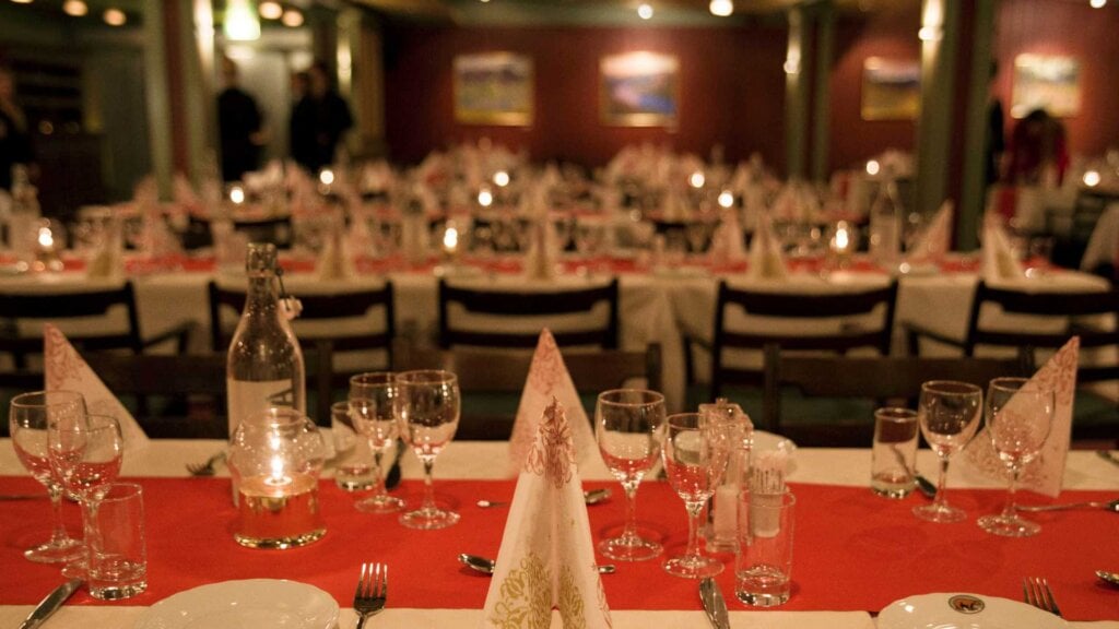 Oppdekking for middag med hvite duker, glass, lys og servietter i en elegant restaurantinnredning.