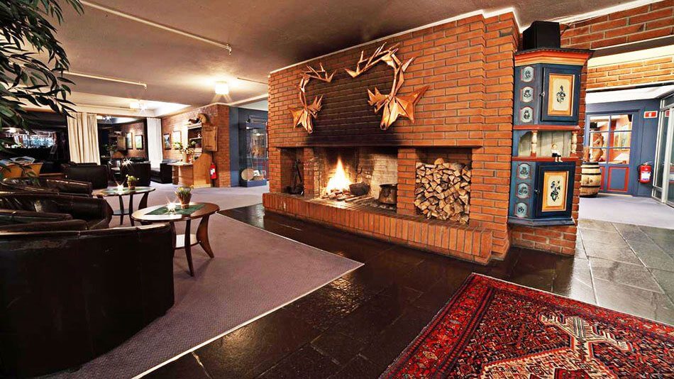 Koselig hotelllobby med stor peis, treved og komfortable sitteplasser for en avslappende atmosfære.