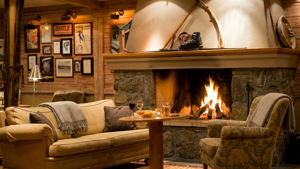 Koselig stue med peis, sofa, og stoler dekorert med tepper, perfekt for avslapning ved bålet på hytta.