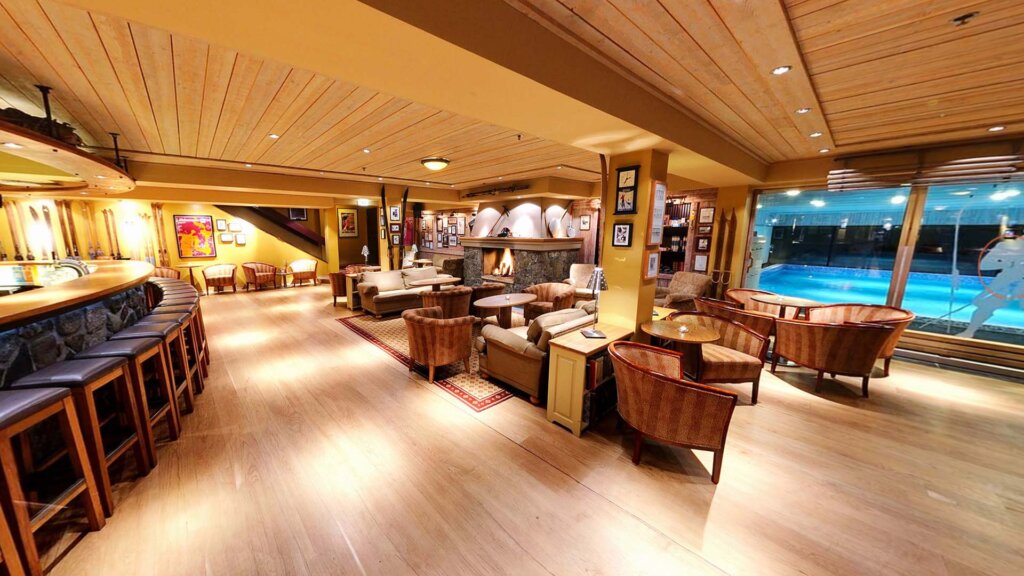 Moderne bar med peis og sittegrupper, utsikt mot svømmebasseng. Koselig interiørdesign i varme toner.
