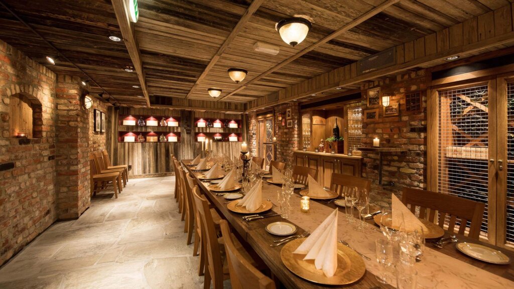 Koselig restaurant med langbord, steinvegger og varm belysning, klar for en intim middag.