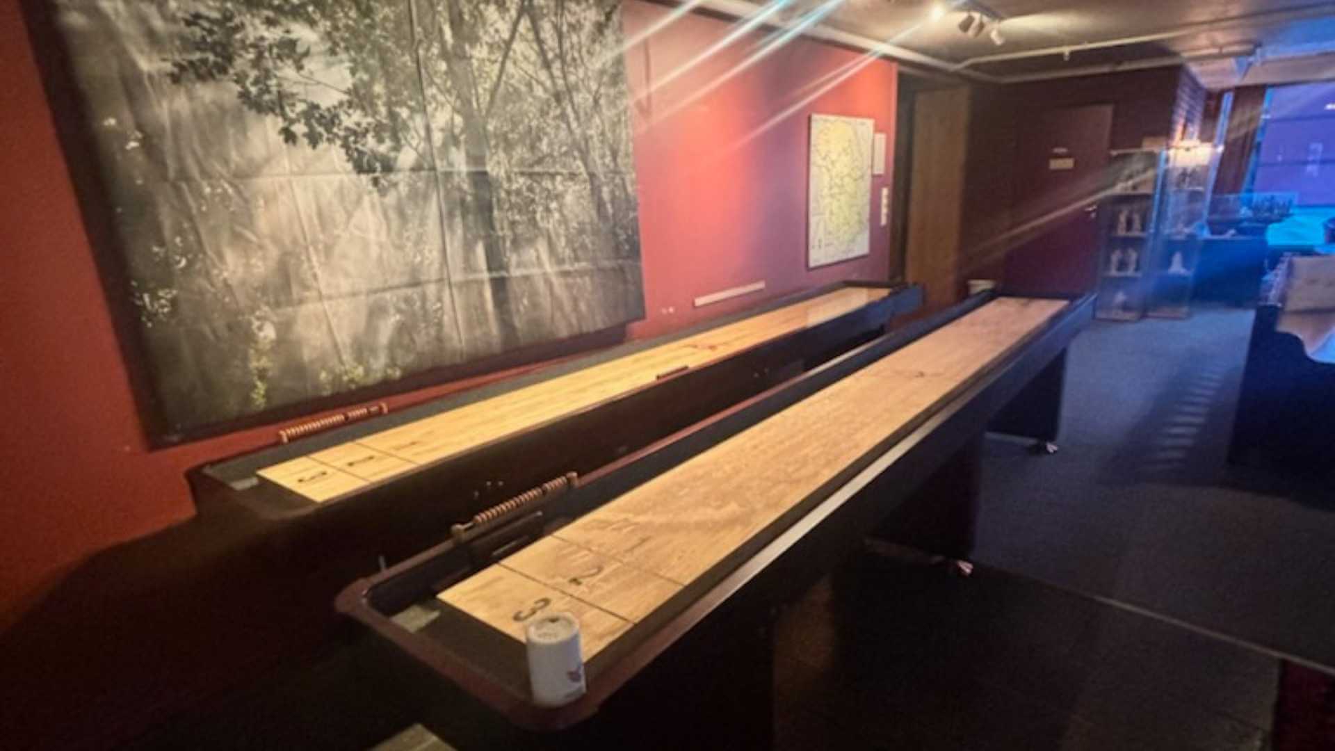 Bord for shuffleboard i en koselig bar med røde vegger og kunstverk på veggen. Perfekt for spillkvelder med venner.