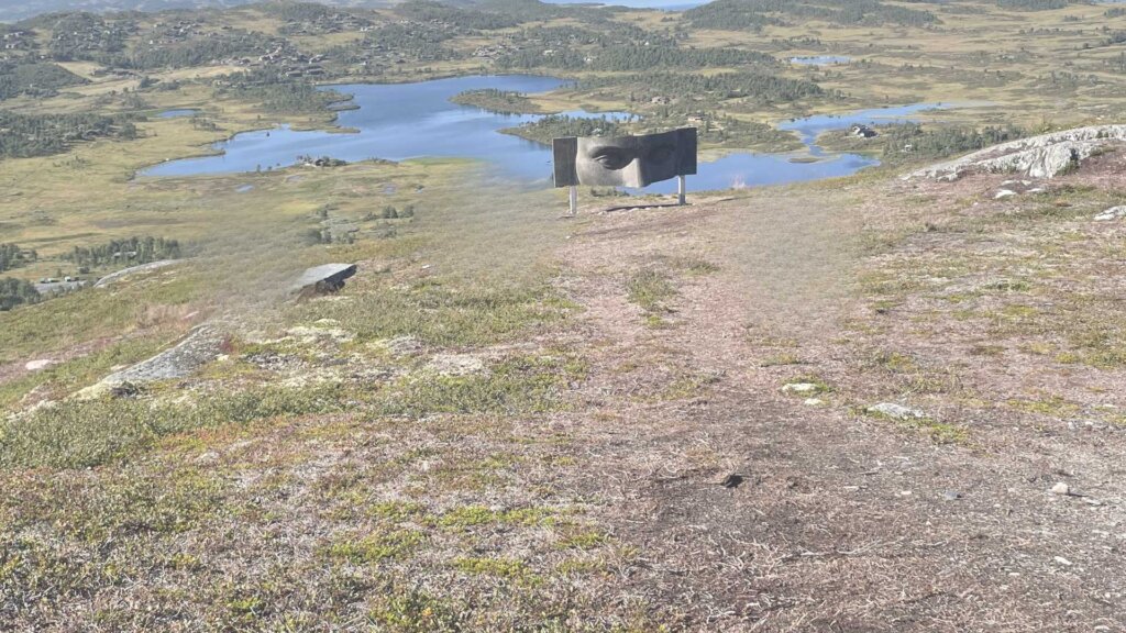 Bilde av en skulptur av et ansikt som stikker opp fra en tursti med vakker utsikt over landskapet.