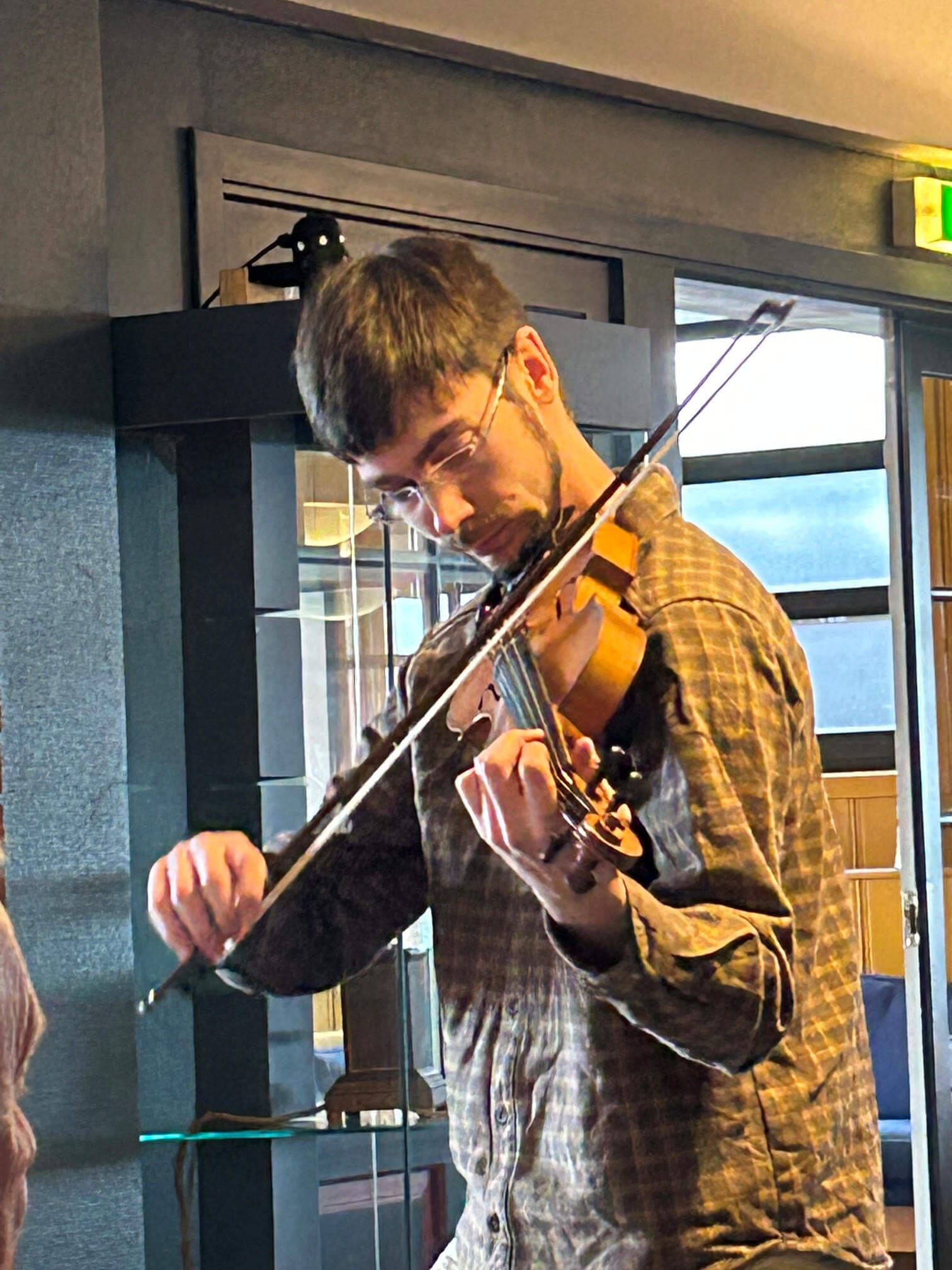 En mann spiller fiolin i et stilfullt rom, fokusert på musikken med et nærbilde av hendene hans.