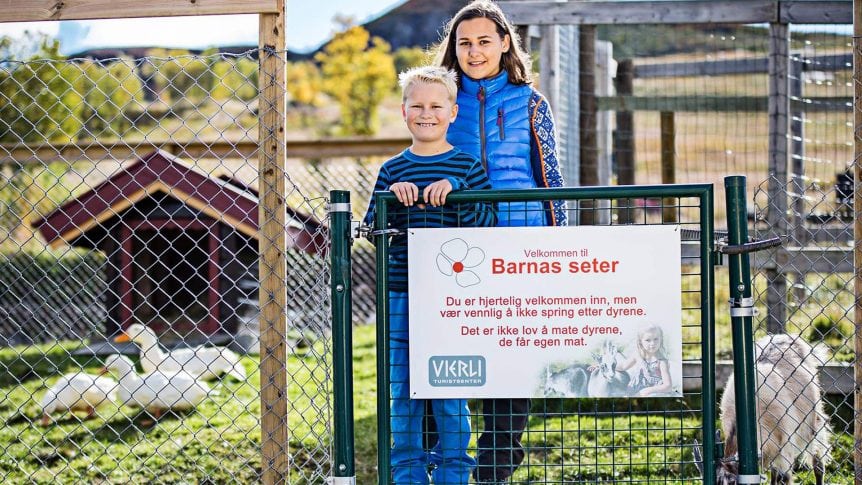 Barn foran inngangen til barnas seter på Vikørli Turistsenter, med advarsel om ikke å løpe etter dyrene.