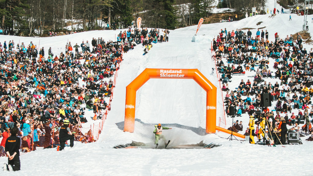Skiløper i fargerik drakt krysser finishlinjen ved Rauland Skisenter, omgitt av engasjerte tilskuere.