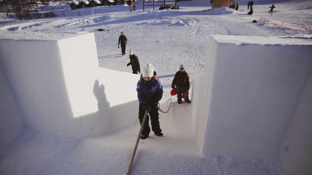 Barn leker i snøen med akebrett i vinterlandskap. De går opp en snøbakke ved hjelp av et tau.