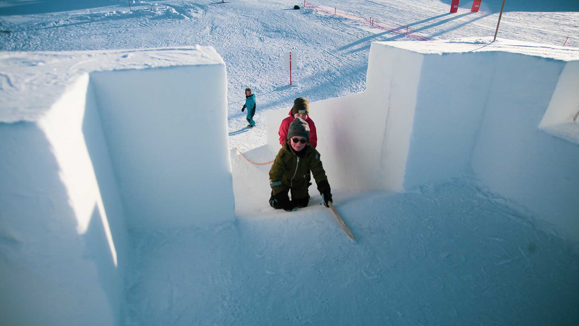Barn klatrer opp snøbakke ved hjelp av tau på solrik vinterdag. Skiglede i snørike omgivelser.