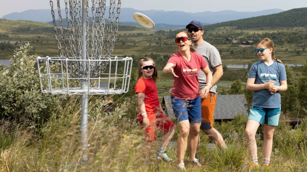 Familie nyter frisbee-golf i naturskjønne omgivelser på fjellet, med fokus på målkurv.