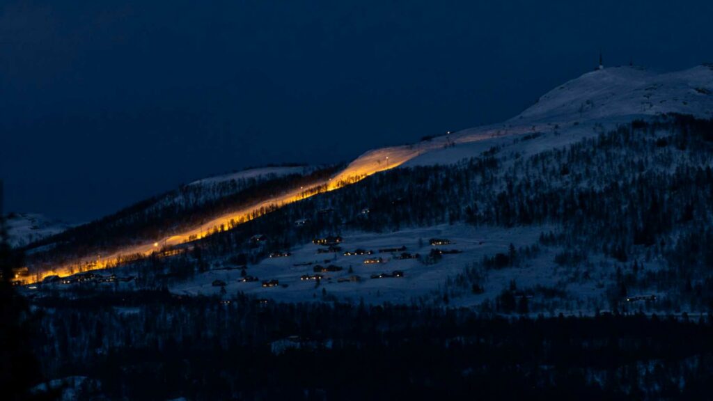 Lys i en fjellandsby om natten, med opplyste hytter og en skiheis som lyser opp den snødekte fjellsiden.