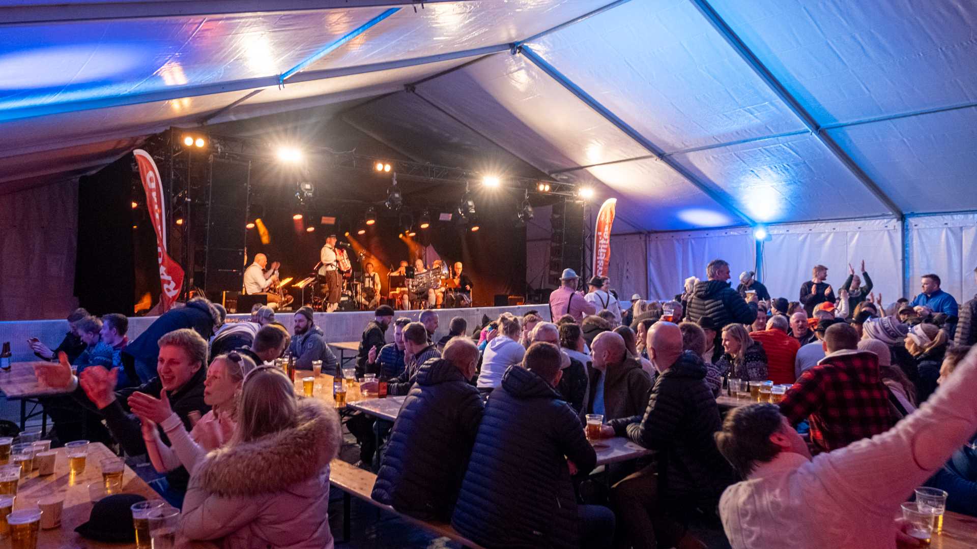 Folkemengde nyter konserten i et opplyst telt, mens bandet spiller på scenen under en festival.