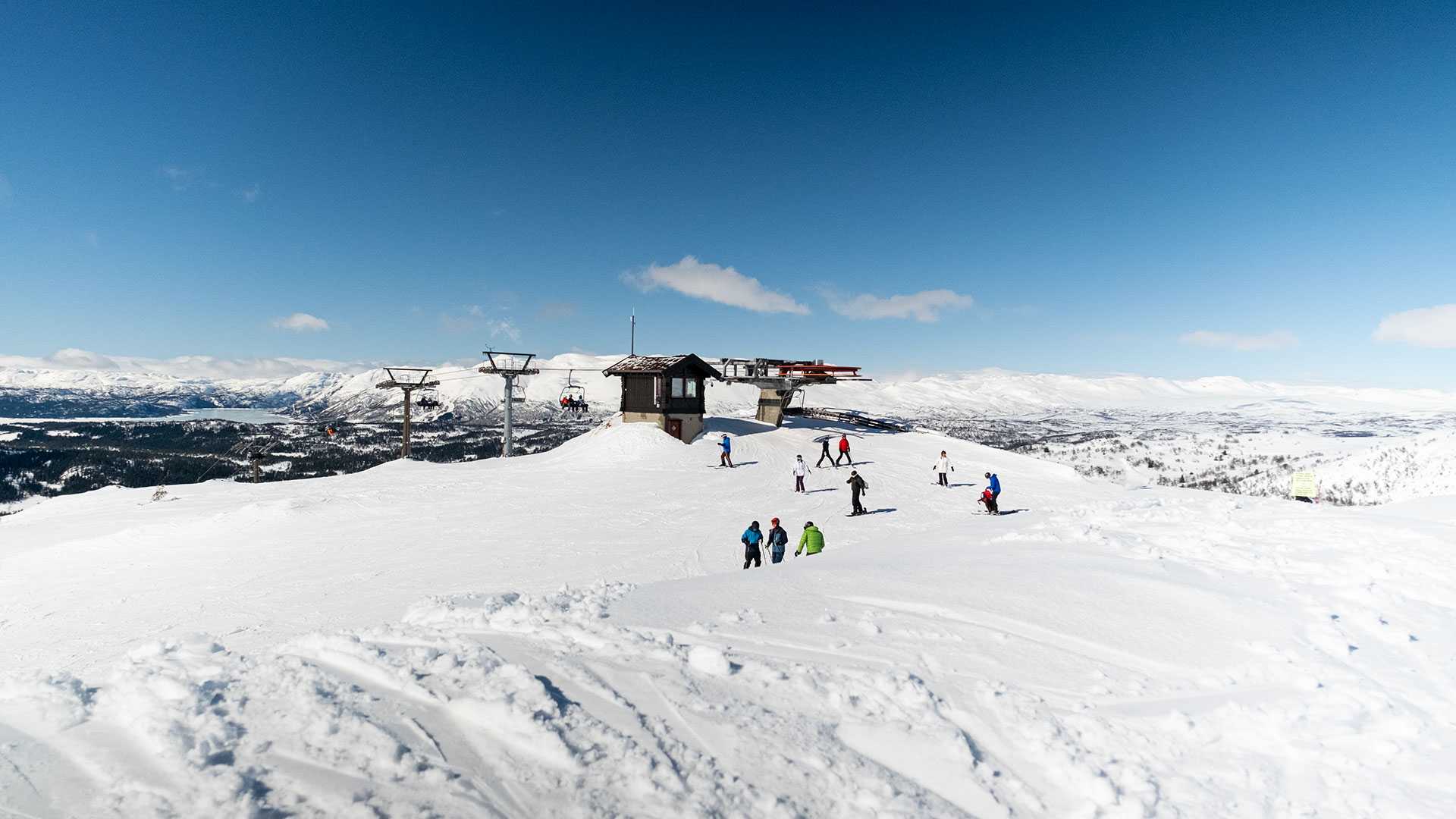 Skiområde med snø, skiheis og skiløpere under en klar blå himmel i et vinterlandskap i Norge.