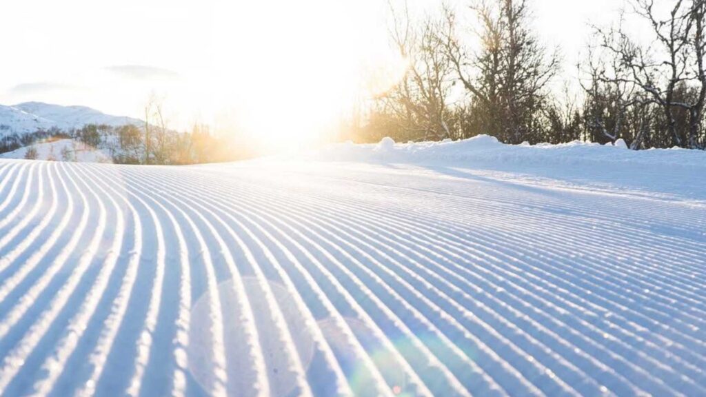 Soloppgang over snødekt landskap med preparerte skispor i vinterlandskap.