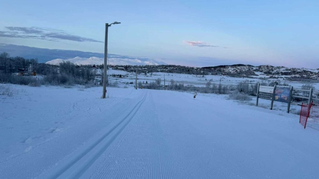 Snødekket landskap med skiløyper og fjell i horisonten under en klar himmel.