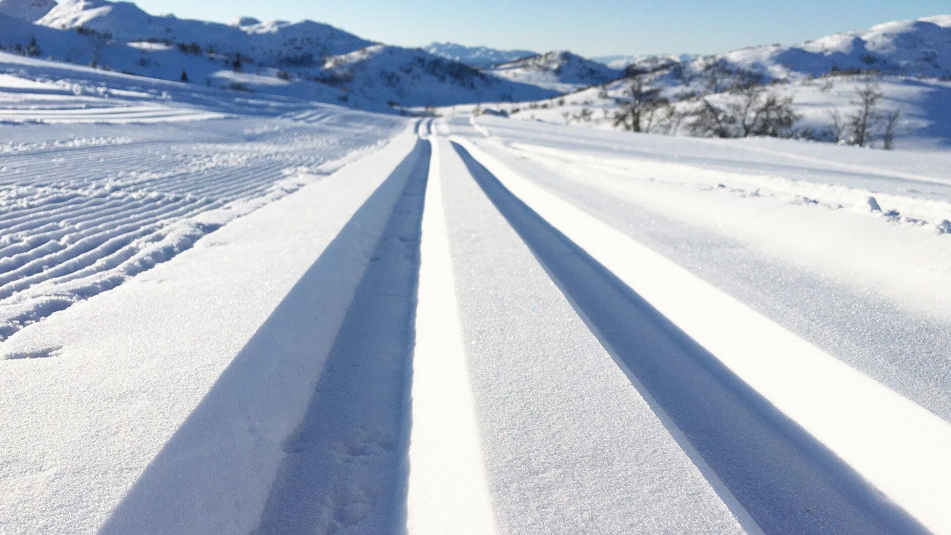 Nypreparerte skiløyper i vinterlandskap, omgitt av snødekte fjell og blå himmel.