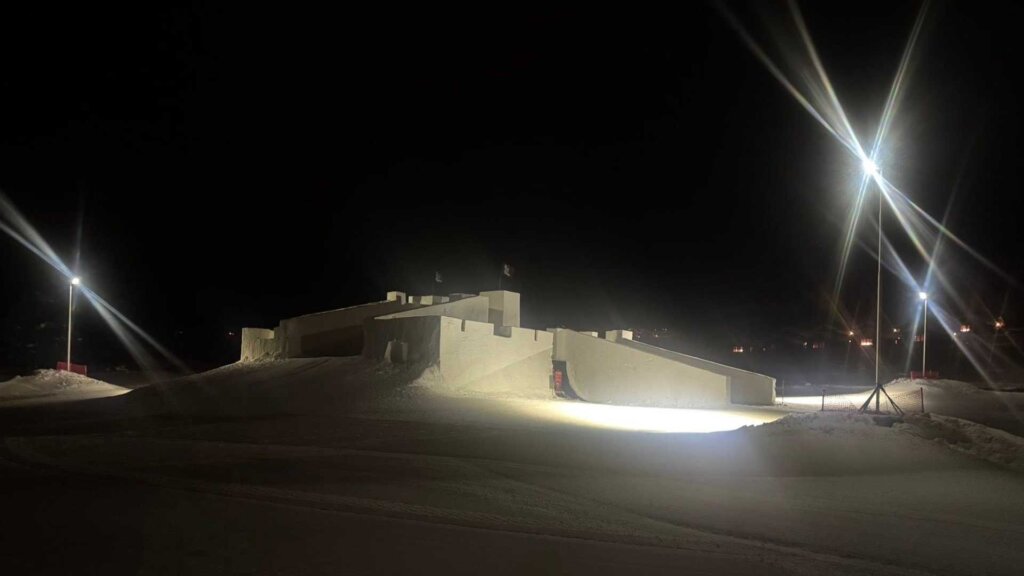 Opplyst snøsculptur som ligner et slott, om natten, med gatelykter som lyser opp området.