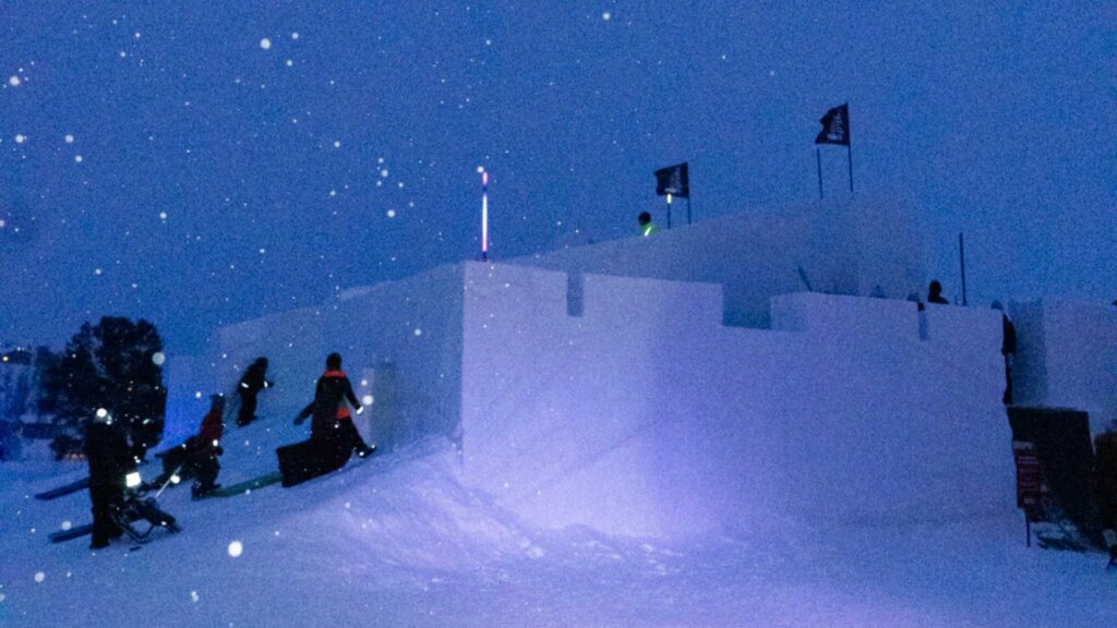 Snø festning om natten med folk som klatrer i snøen og flakkende snøfnugg i luften.