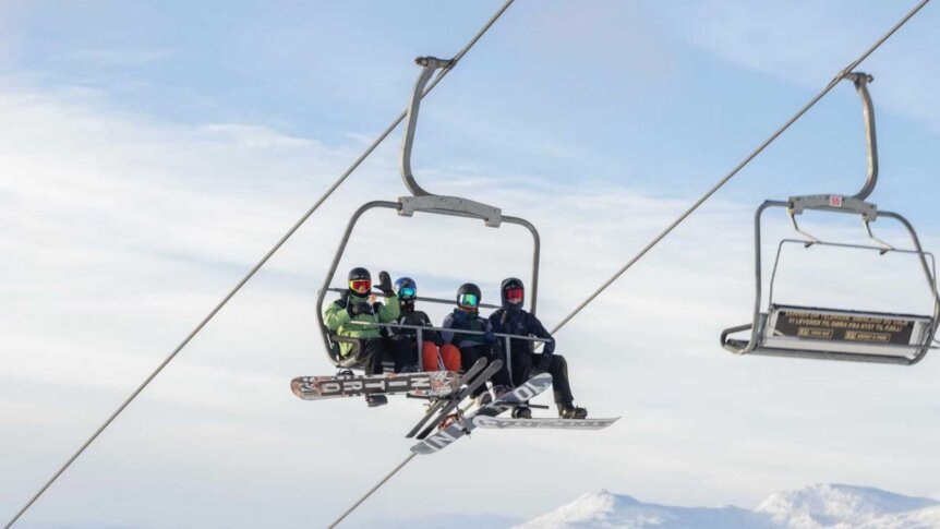 Fire personer i skitrekk med skiutstyr, blå himmel og snødekte fjell i bakgrunnen.