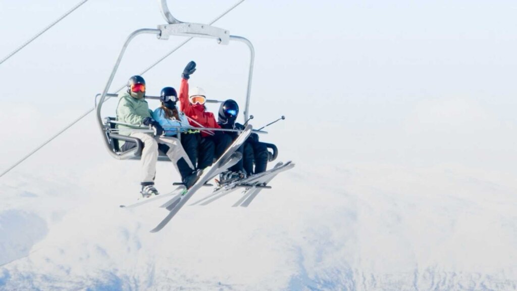 Fire personer på skiheis over snødekte fjell, solfylt dag og vintersport i fokus.