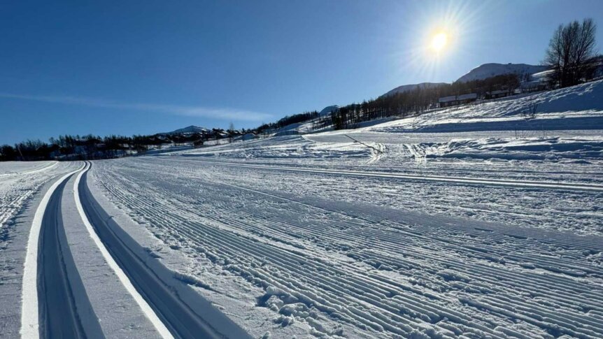 En solfylt vinterlandskap med skiløype og snødekte fjell i bakgrunnen. Perfekt for langrenn og vinteraktiviteter.