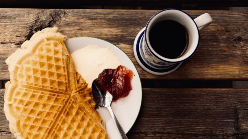 Norske vafler med rømme og syltetøy, servert med en kopp kaffe på et trebord. Perfekt for en koselig stund.