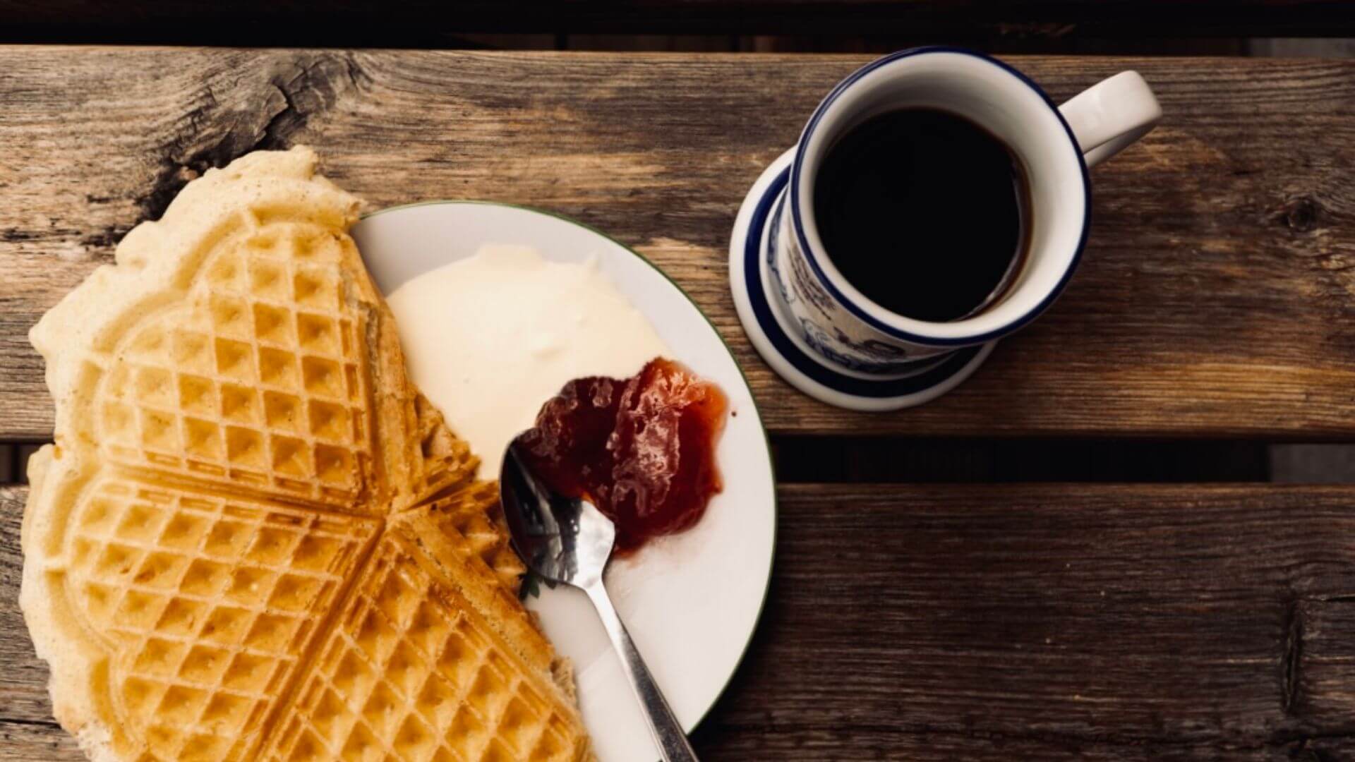 Norske vafler med rømme og syltetøy, servert med en kopp kaffe på et trebord. Perfekt for en koselig stund.