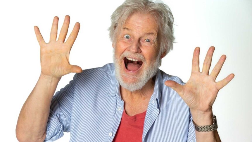 Gammel mann med grått hår, smilende og holder hendene oppe som viser entusiasme og glede.