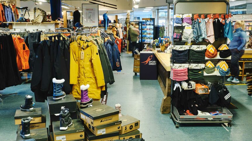 Sportsbutikk med jakker, støvler og tilbehør utstilt for salg. Sport Direkt-logoen er synlig i butikken.
