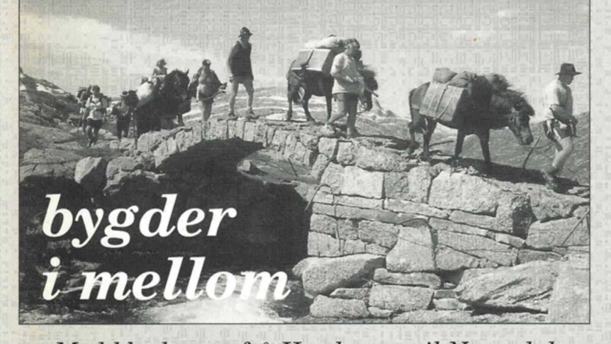 Gruppe vandrer med hester over steinbro i fjellandskap, tekst bygder i mellom. Svart-hvitt foto.