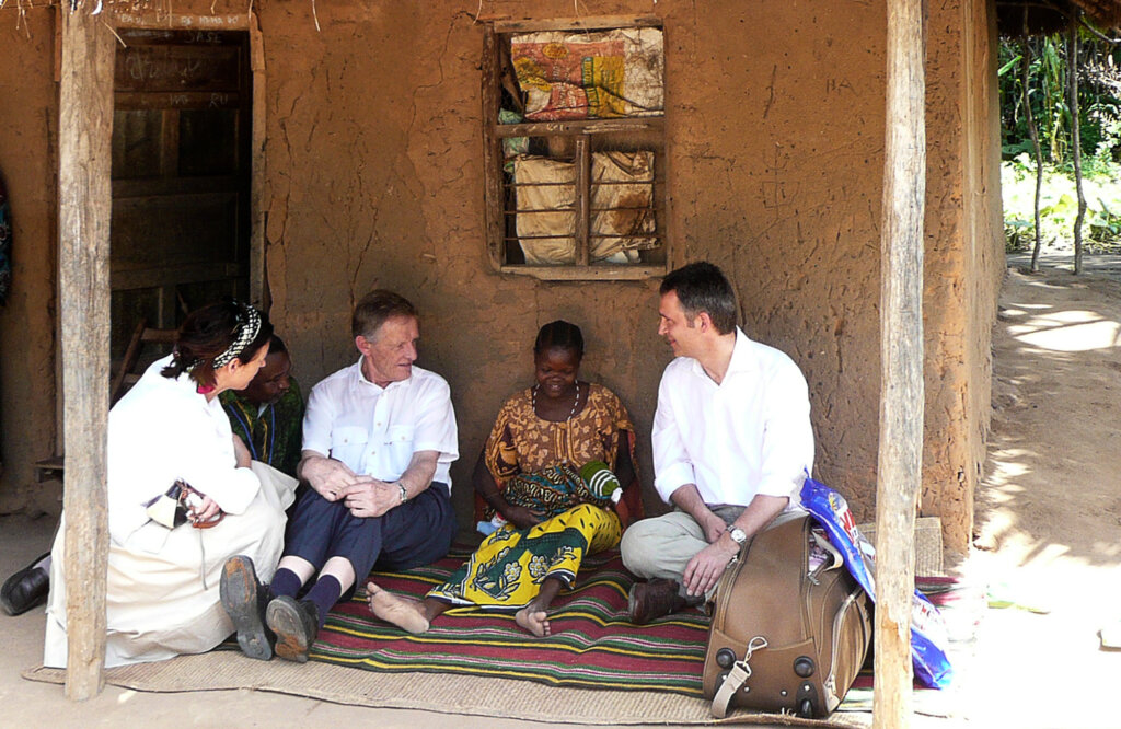 Møte mellom personer utenfor et hus i en landsby, med fokus på samtale og kulturutveksling.