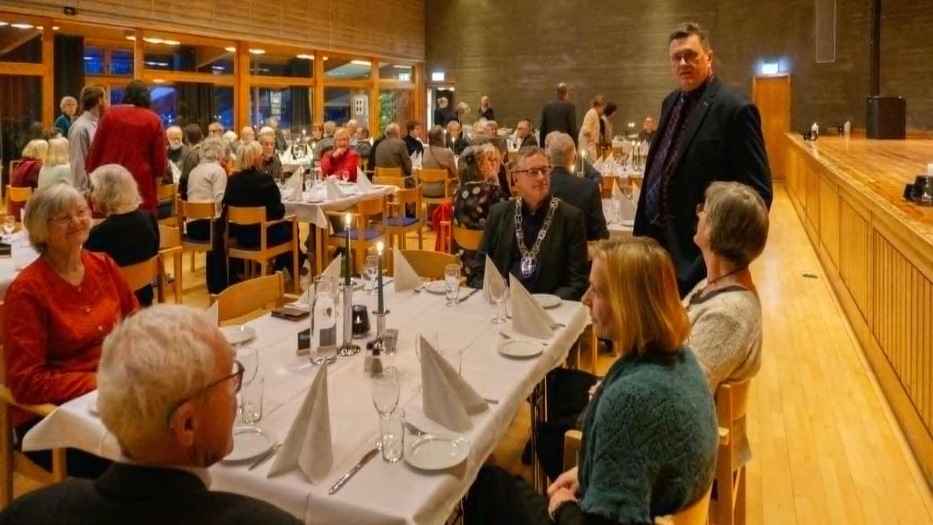 Middag med gjester i en lys restaurant med bord dekket for fest, folk mingler og samtaler.