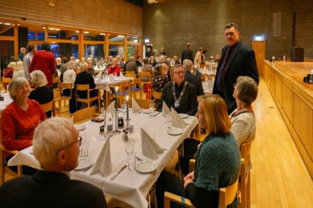 Gjestene nyter en festmiddag i en elegant restaurant, med levende lys og pent dekorerte bord.