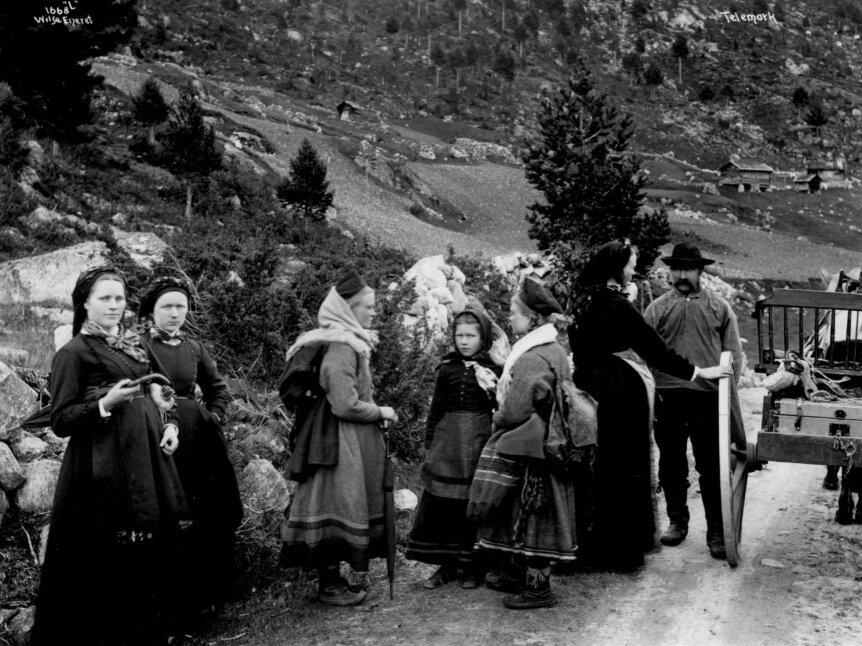 Kvinner og menn i tradisjonelle klær står ved en vei i Telemark, Norge, rundt 1884. Historisk sort-hvitt bilde.